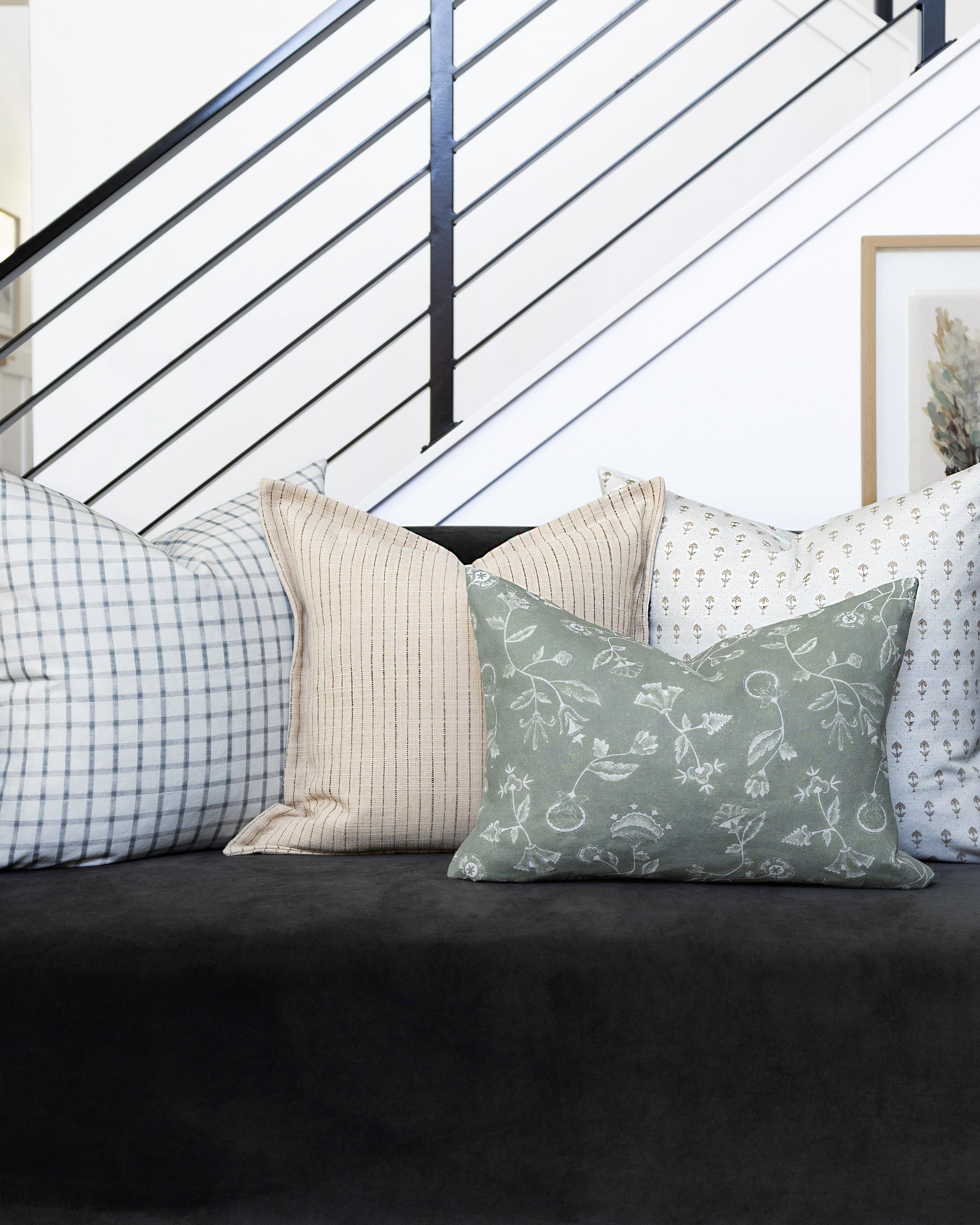 Black sofa with patterned cushions in a room with a staircase and framed picture.