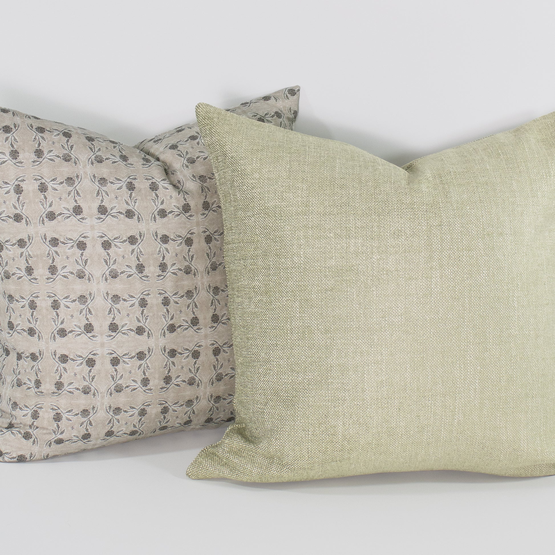 Two pillows, one with a floral pattern and the other plain, on a light background