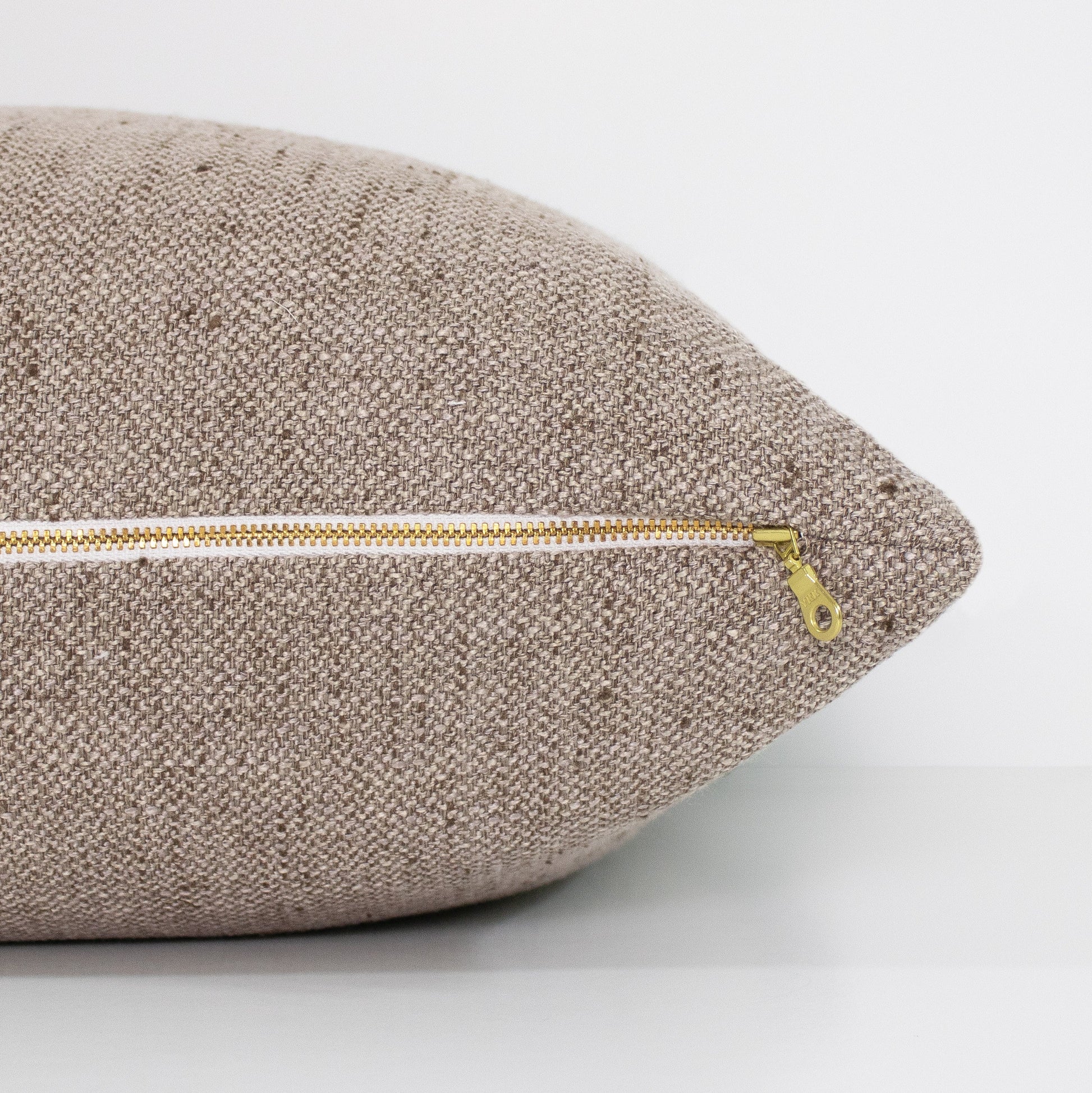 Textured light brown pillow with a gold zipper on a light gray background
