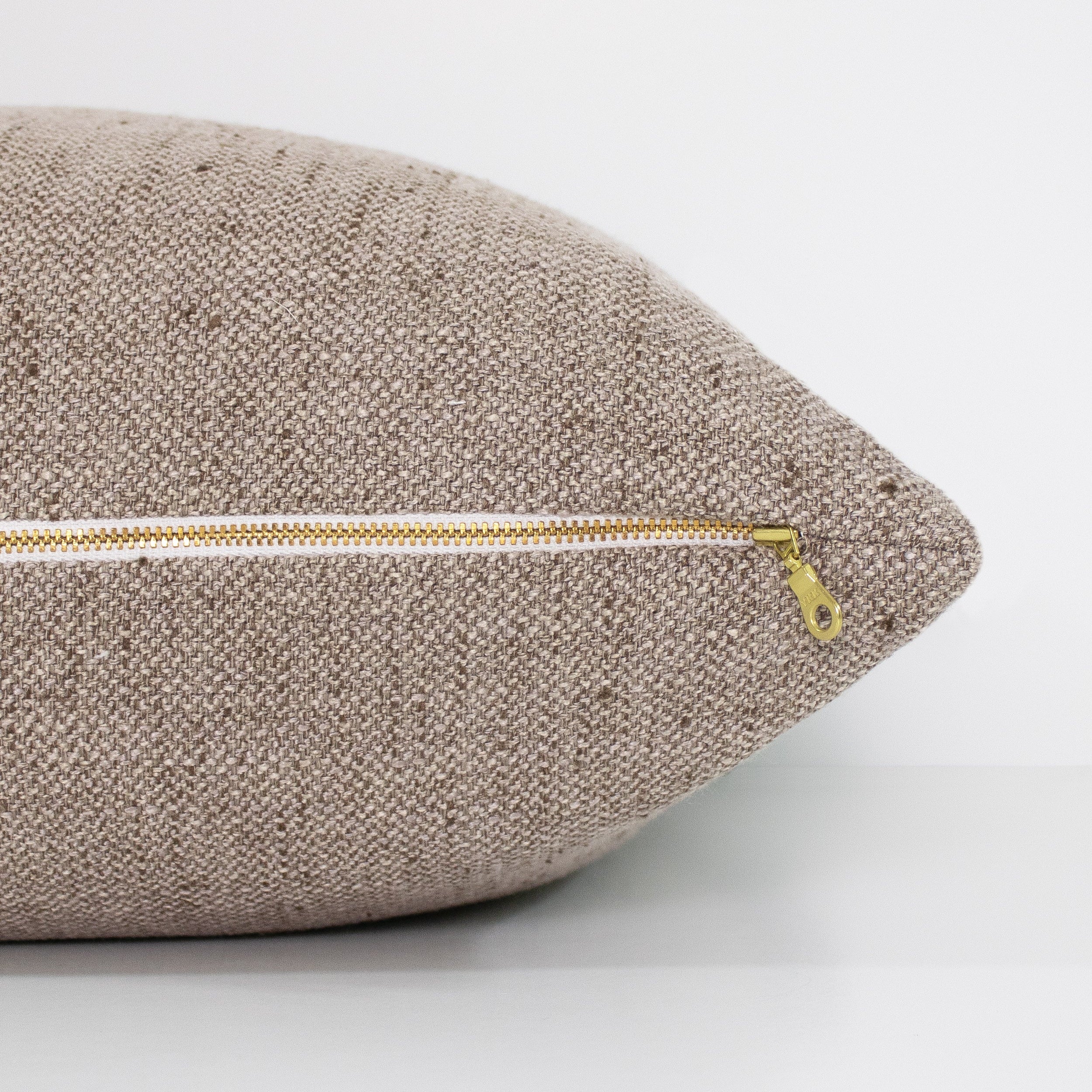 Textured light brown pillow with a gold zipper on a light gray background